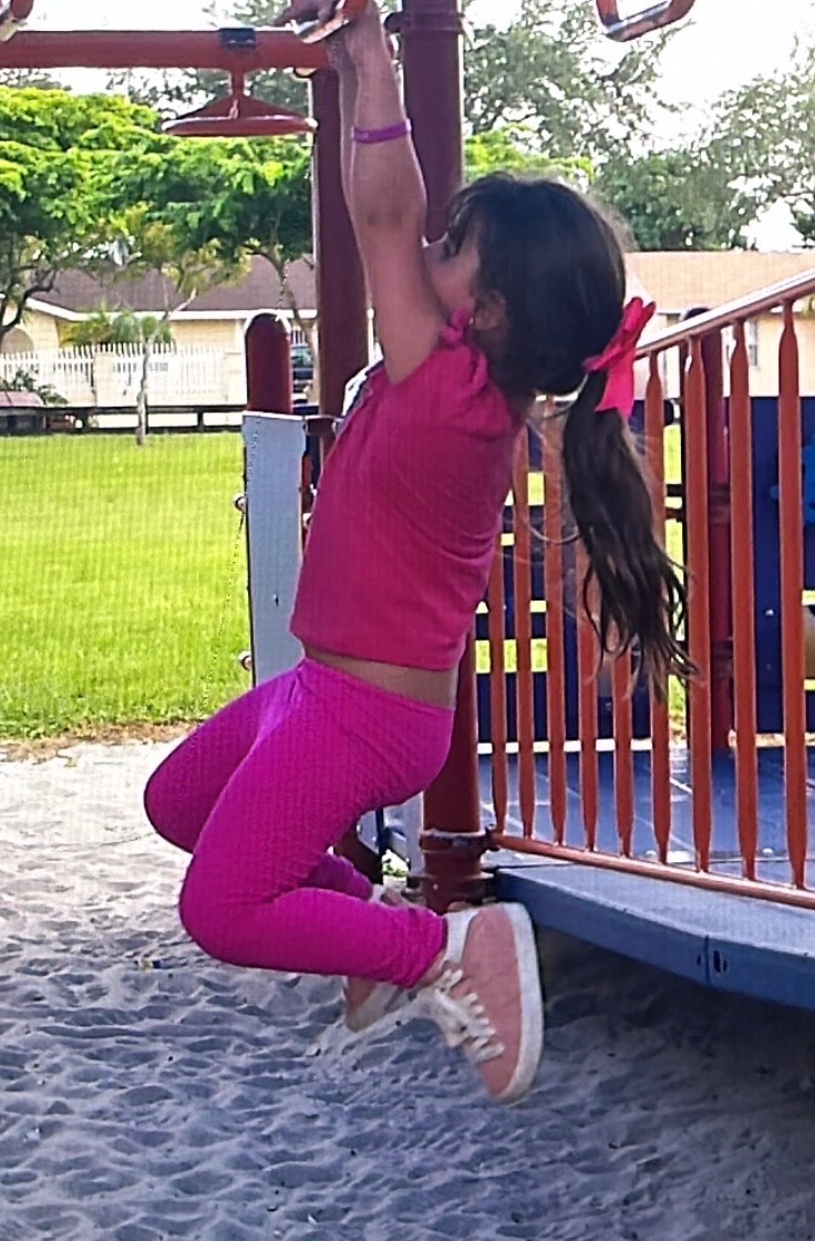 Child hanging from playground monkey bars building upper-body strength